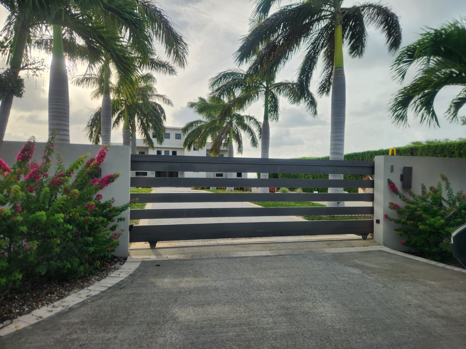Charcoal grey horizontal slat sliding gate framed by royal palms and bougainvillea in Anguilla