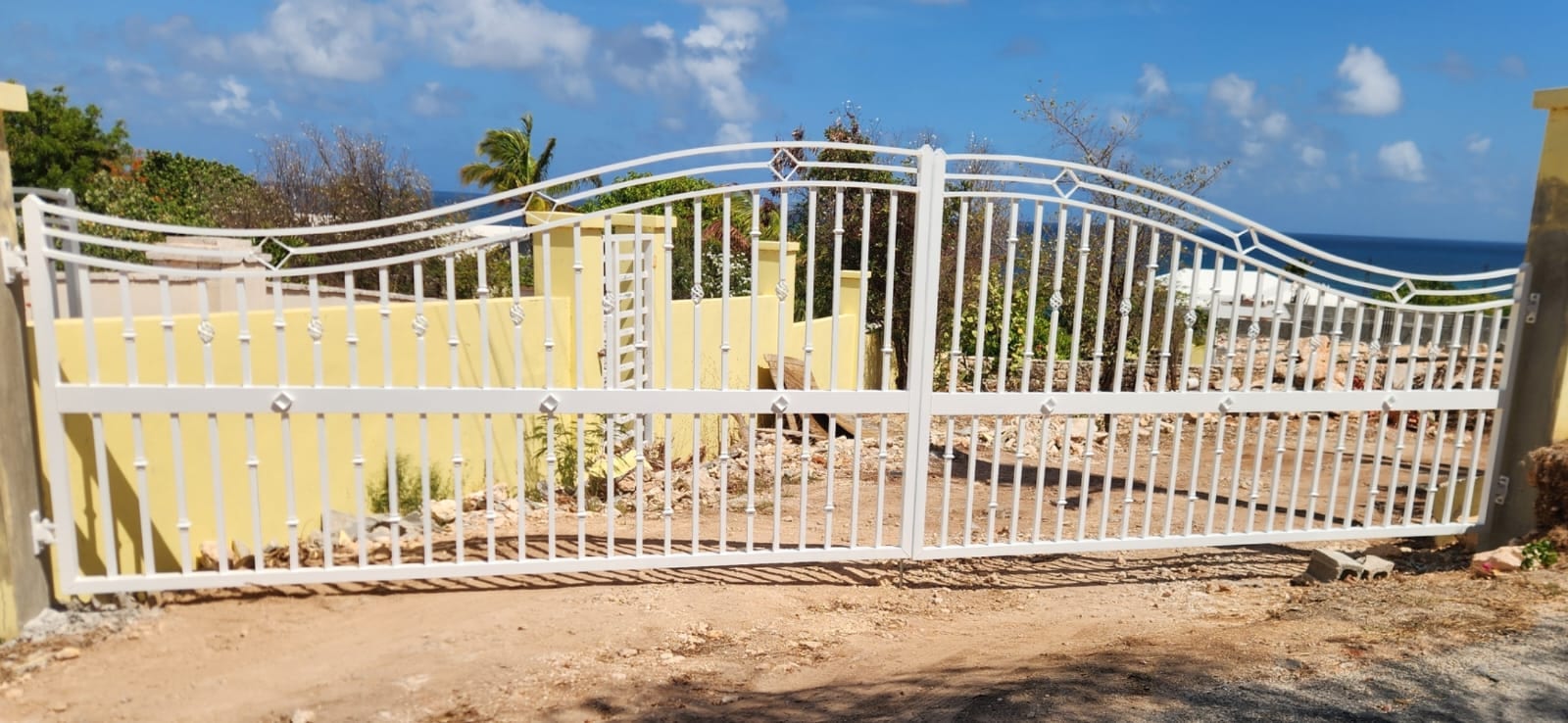 White aluminium driveway gate with a curved top rail and diamond detail overlooking the sea in Anguilla