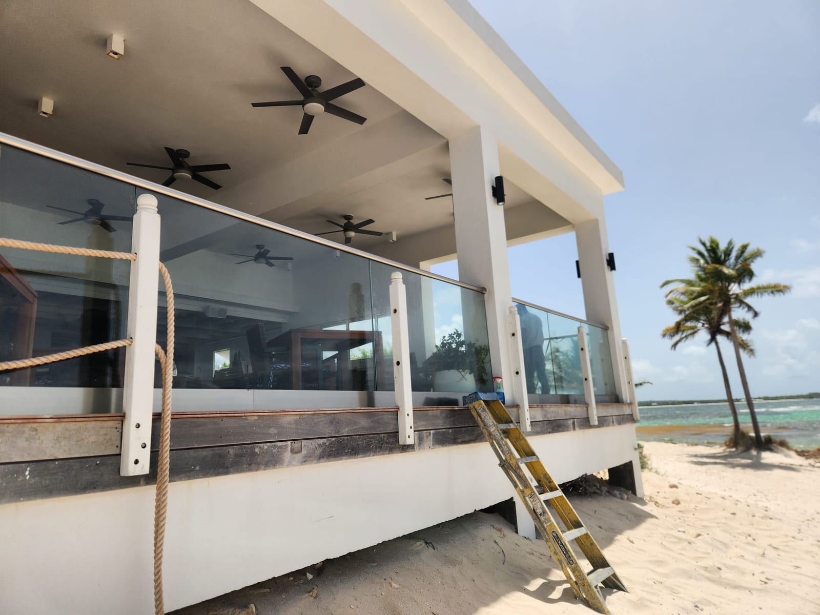 Glass balustrade running along a beachfront deck beside palm trees in Anguilla