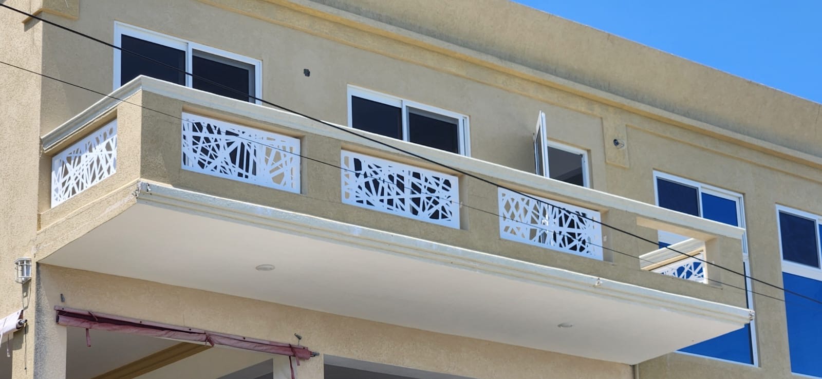 White laser-cut aluminium balcony railing panels with an abstract branch pattern on a building in Anguilla