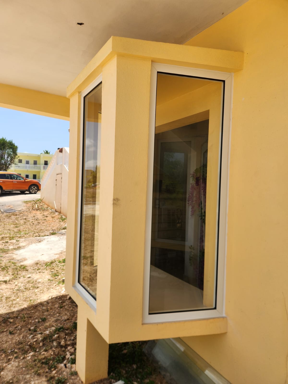 Close-up of a white-framed aluminium corner bay window fitted to a yellow rendered wall