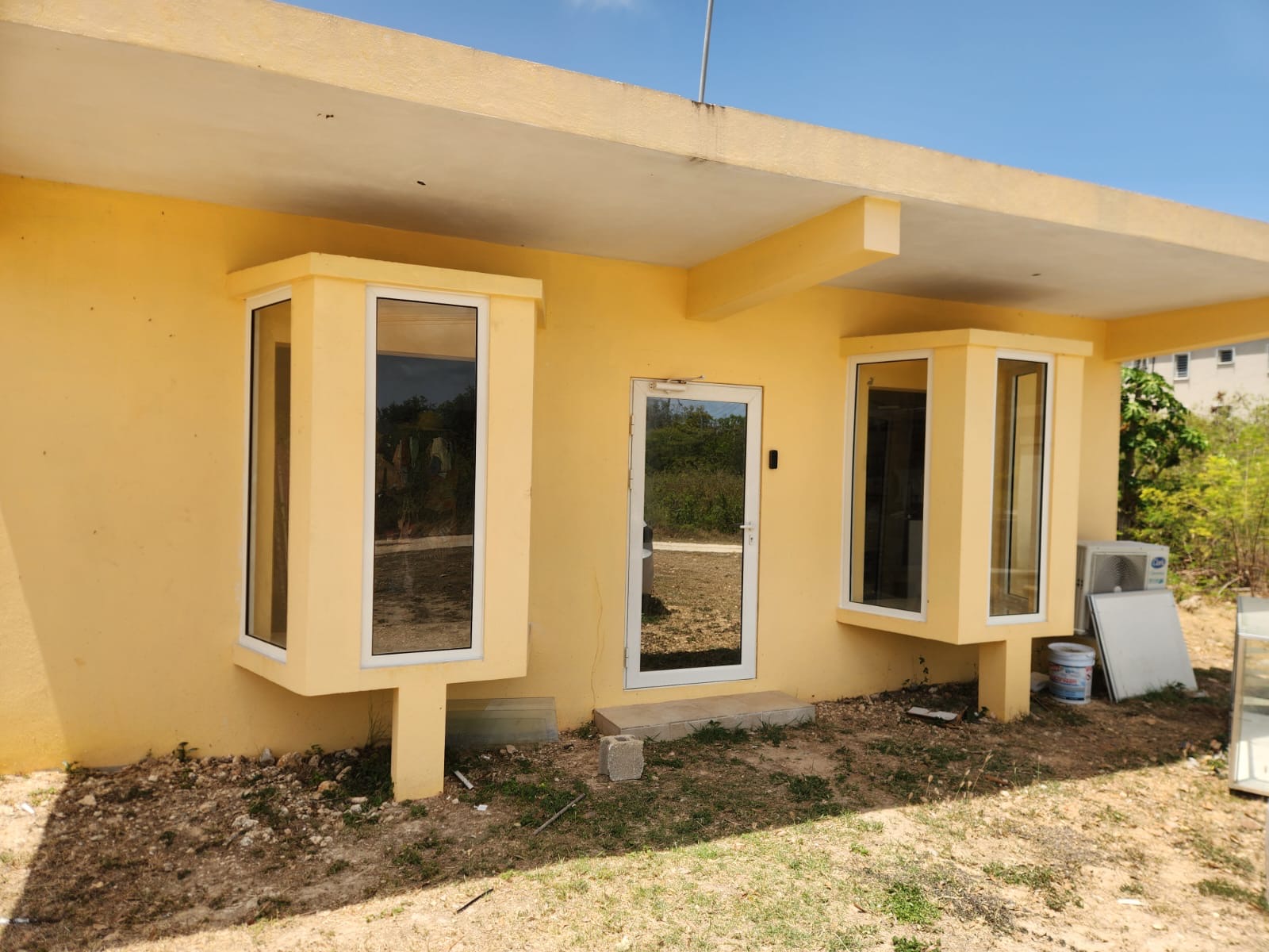 White aluminium bay windows and a glass entry door installed on a yellow building in Anguilla
